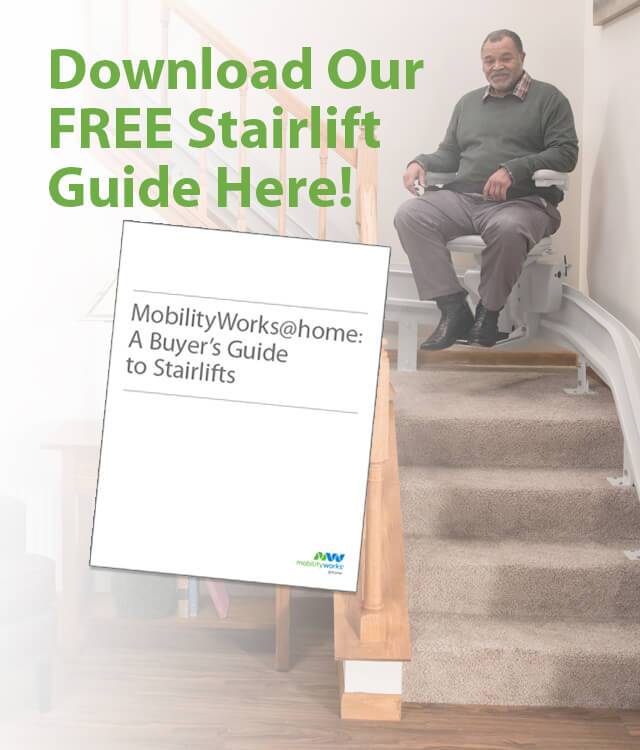 A man sits on a stairlift at the top of a staircase. Text reads Download Our Free Stairlift Guide Here with an image of the guide titled MobilityWorks@home: A Buyer’s Guide to Stairlifts.