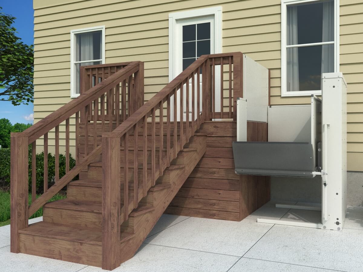 bruno-platform-lift-mid-way-no-gate-90-degree A wooden staircase outside a house stands next to a mechanical lift, designed for accessibility, positioned on a concrete surface.