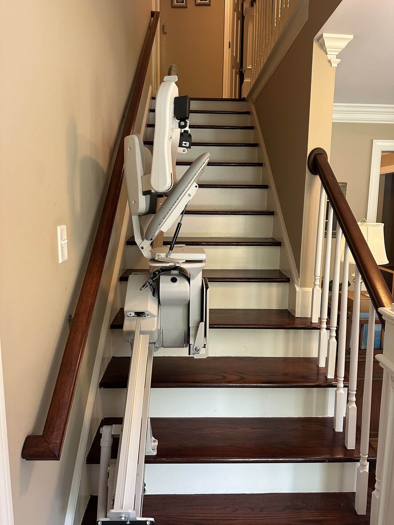 A stair lift installed on a wooden staircase with beige walls and a wooden bannister.