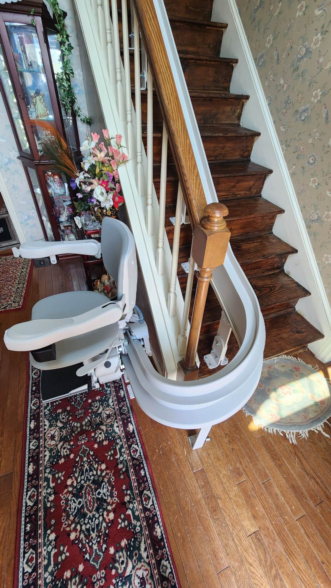 A stairlift installed alongside a wooden staircase with floral decorations nearby.