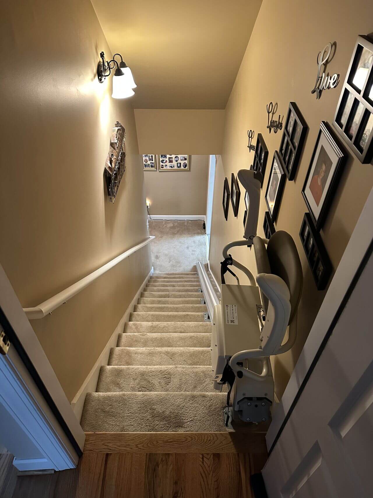 A carpeted staircase with a chair lift installed on the railing, surrounded by picture frames on the walls.