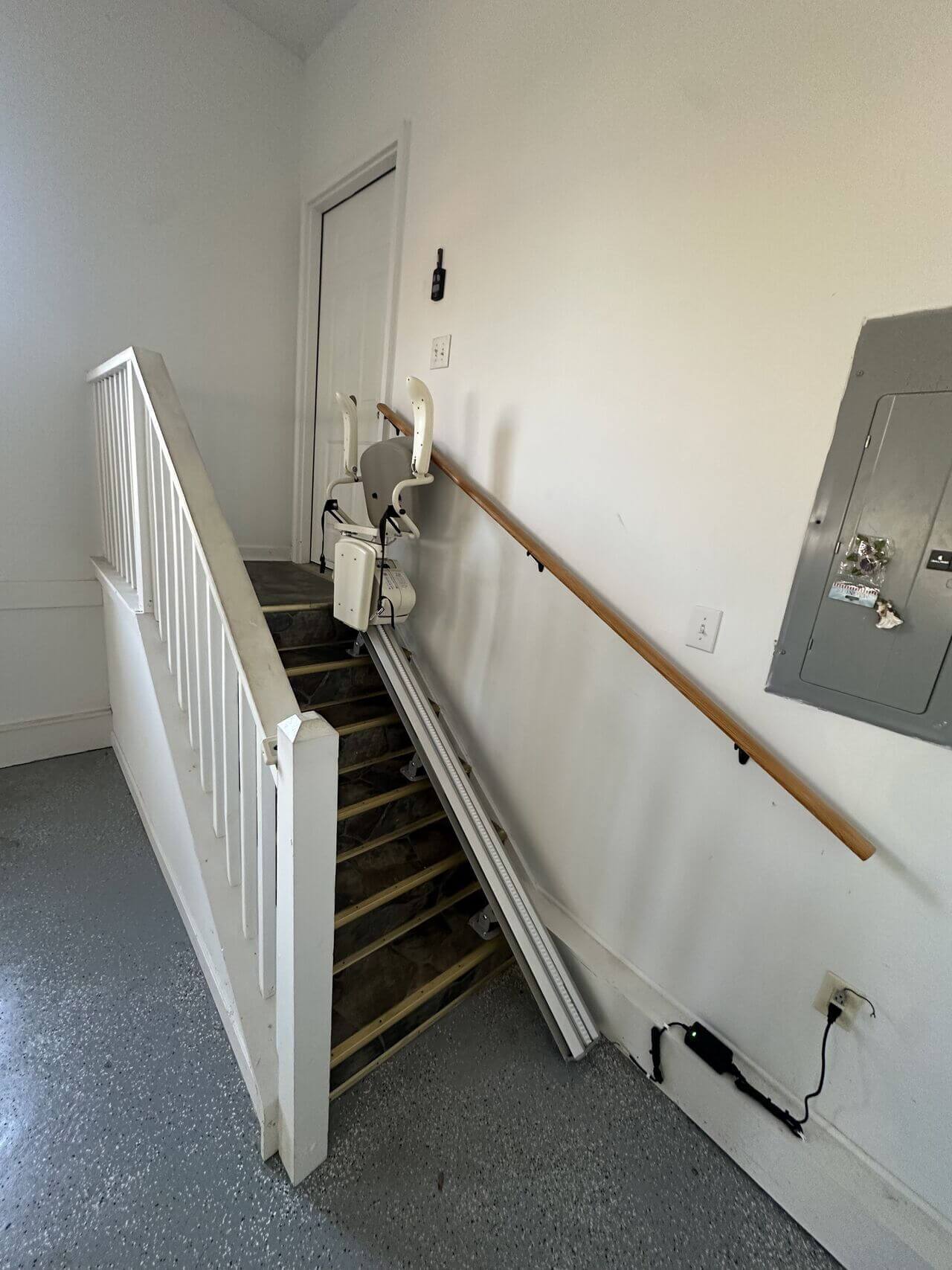 A stairlift installed on a staircase with a wooden handrail in a hallway, adjacent to a closed door.