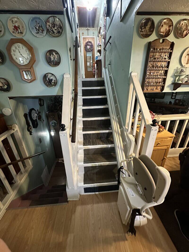 A narrow stairway with a stairlift chair, decorated with clocks and framed pictures on the walls.
