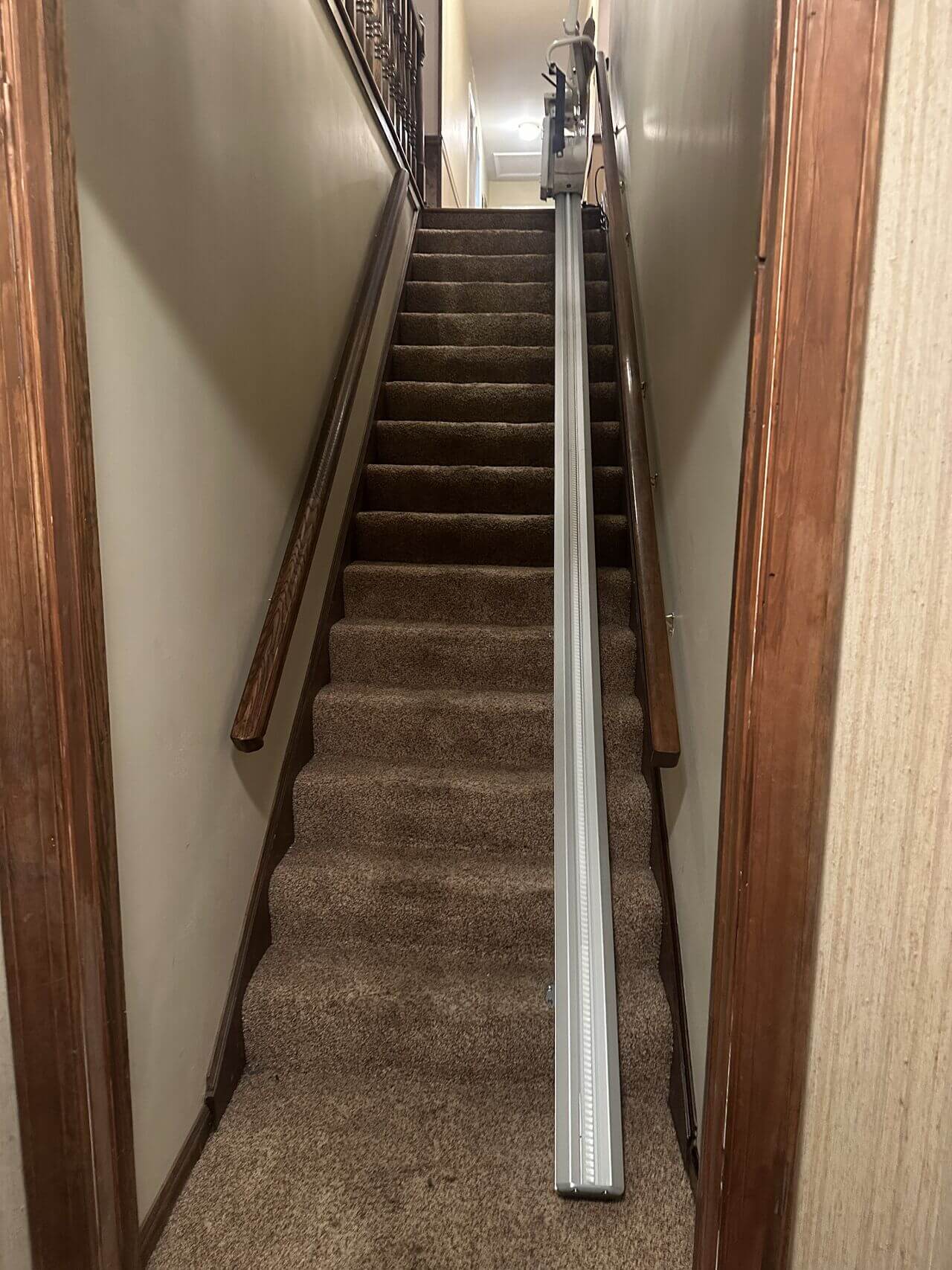 Carpeted stairway with a stair lift track installed on the right side, wooden handrails on both sides.