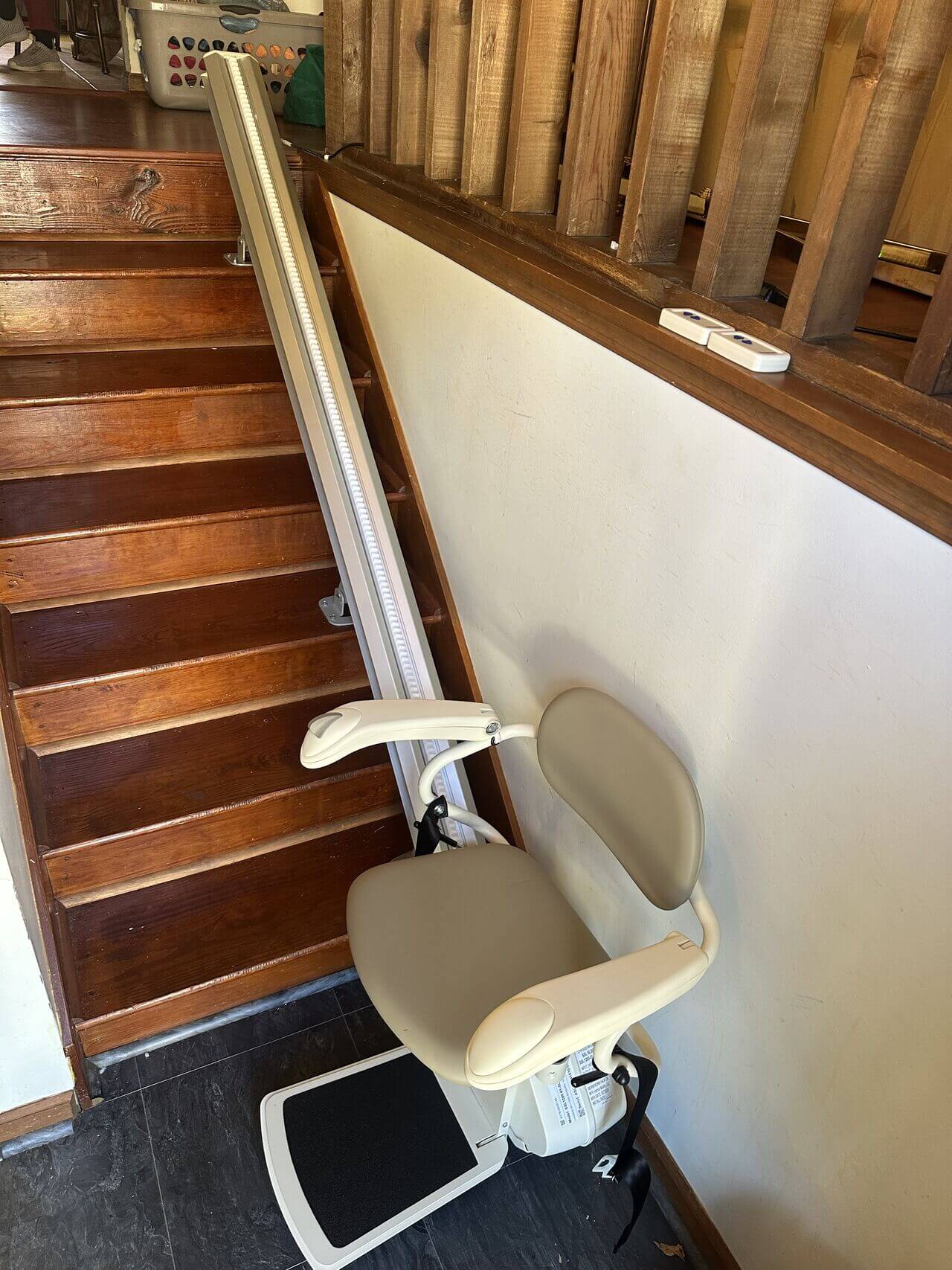Stair lift chair installed on a wooden staircase with a beige seat and safety belt.