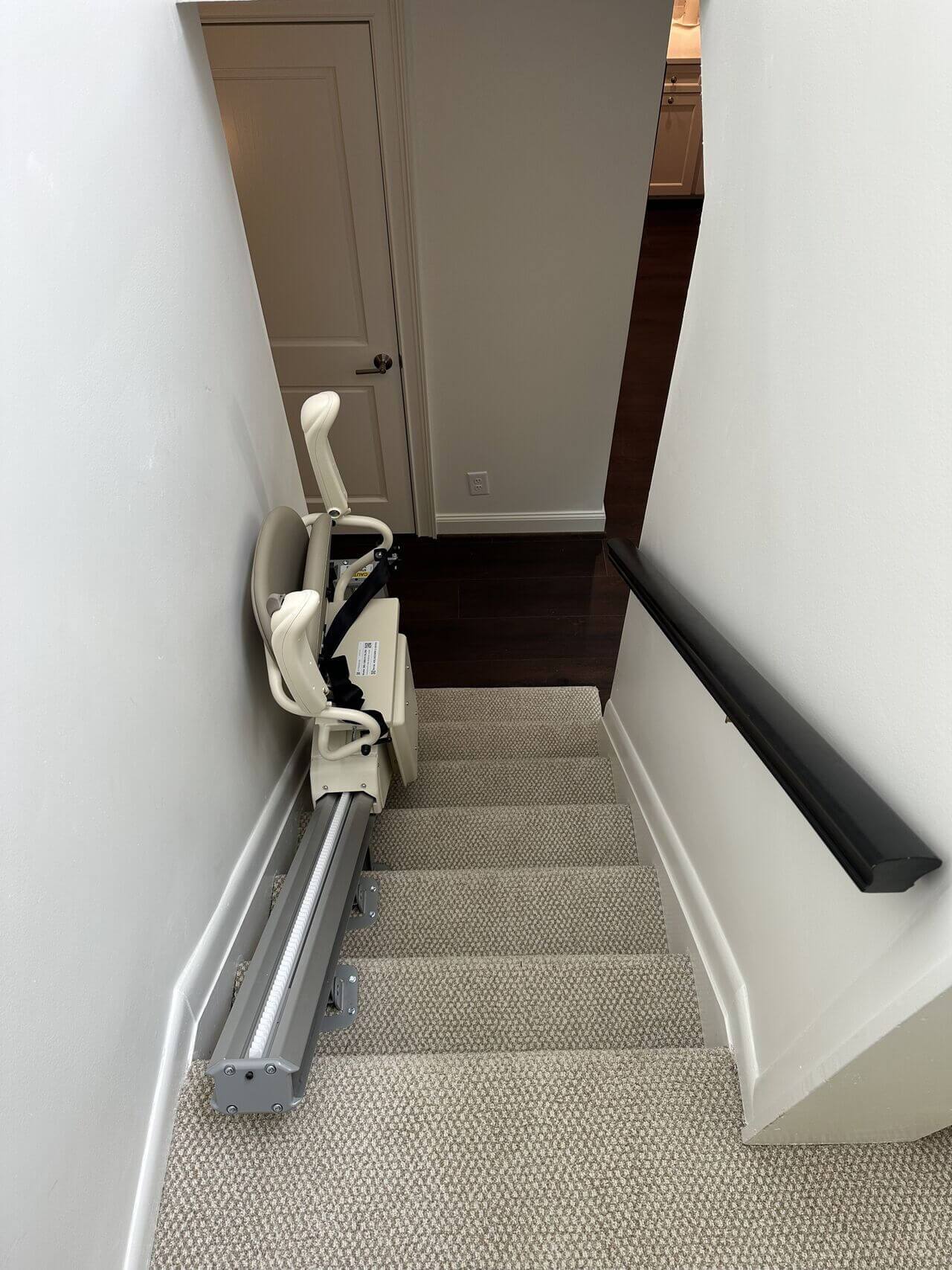 Staircase with a stairlift installed on the left side, leading down to a closed door.