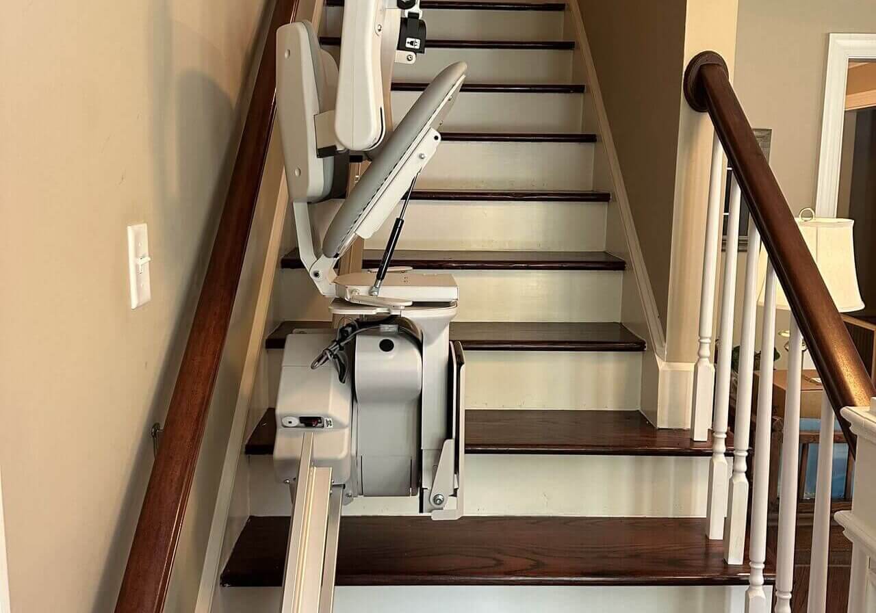 A stair lift installed on a wooden staircase with beige walls and a wooden bannister.