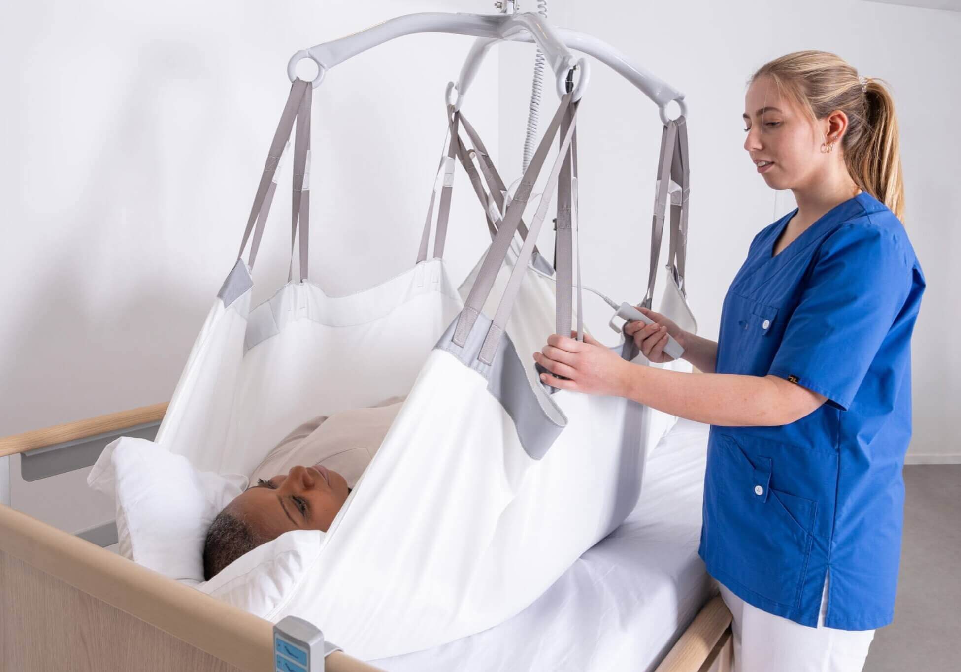 A healthcare worker operates a patient lift device, aiding a person in bed.