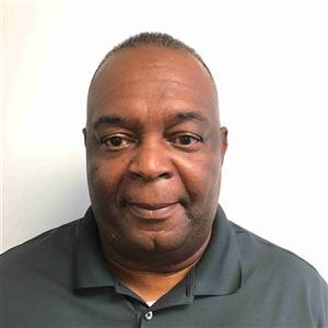 A man with short hair stands confidently against a plain white background, clad in a dark polo shirt. His poised demeanor subtly embodies the spirit of MobilityWorks, highlighting the synergy between style and accessible innovation.