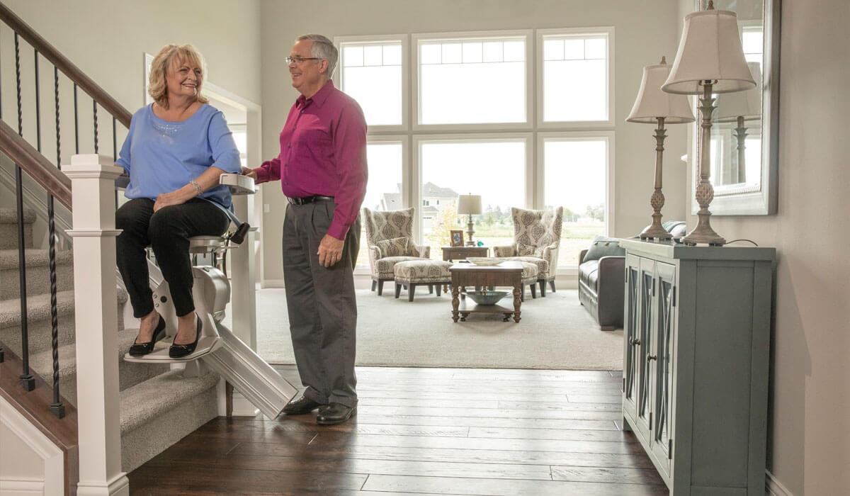 Woman on stair lift with man standing next to herWoman on stair lift with man standing next to her