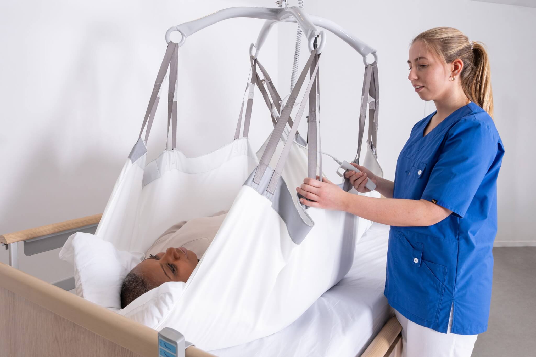 A healthcare worker operates a patient lift device, aiding a person in bed.