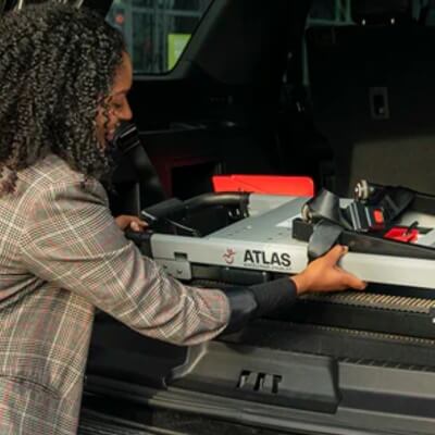 A person efficiently places an ATLAS foldable wheelchair, a perfect companion for the mobile stairlift, into the trunk of a vehicle.