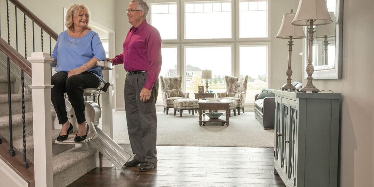 Woman on stair lift with man standing next to herWoman on stair lift with man standing next to her